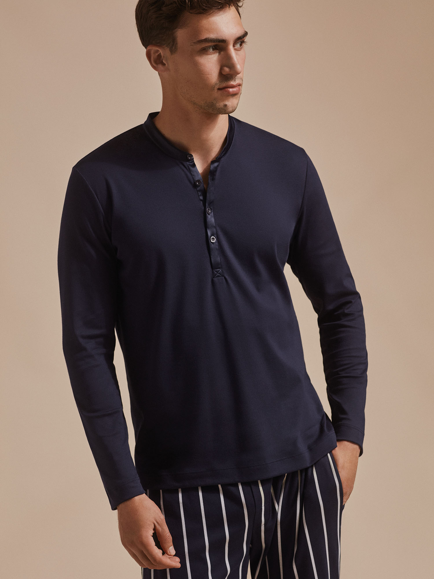 Male model stands in Henley long-sleeved pajama shirt and striped trousers | mey® 